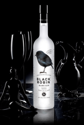 A bottle of Black Robin Rare Gin centered against a black background, flanked by two black wine glasses and dark decorative figures. The bottle is frosted white with a black bird illustration and the text 'BLACK ROBIN RARE GIN' on the label.